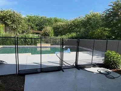 Black mesh pool safety fence with self-closing gate around concrete pool deck