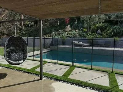 Black mesh pool safety fence around in-ground pool with concrete deck and landscaping